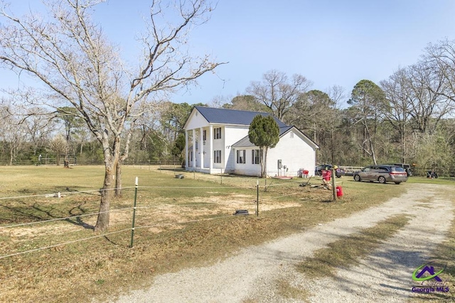 colonial-style house featuring dirt driveway, fence, and a front lawn