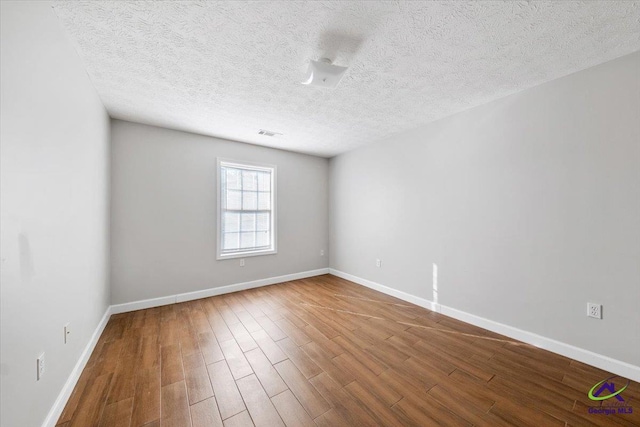 spare room with a textured ceiling, baseboards, and wood finished floors