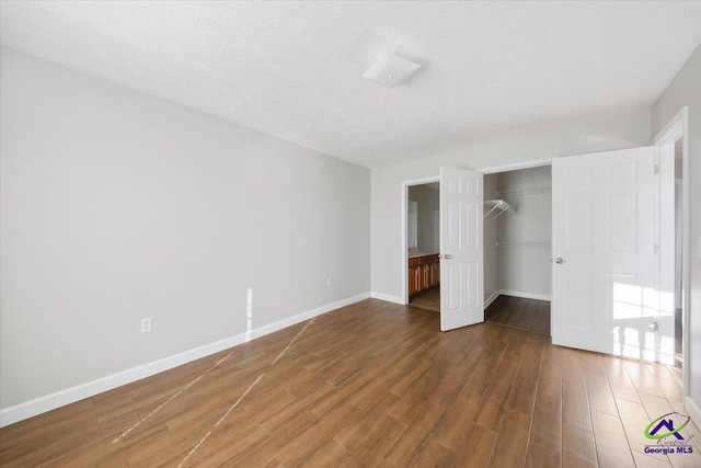 unfurnished bedroom featuring a textured ceiling, dark wood-style flooring, baseboards, a spacious closet, and a closet