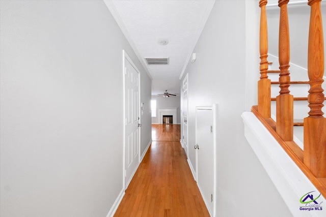 hallway with baseboards, visible vents, a textured ceiling, and light wood finished floors