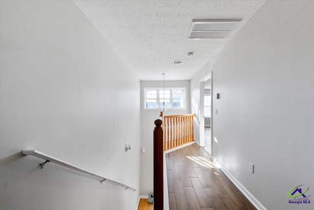 hall featuring a textured ceiling, visible vents, dark wood-type flooring, and an upstairs landing