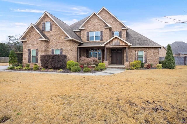 view of front facade with brick siding, a front yard, fence, and a shingled roof