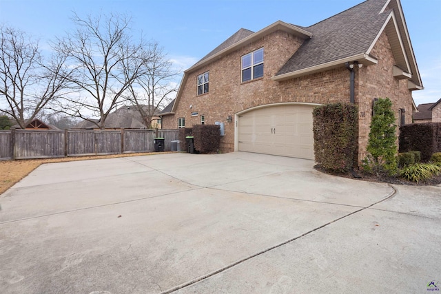 view of side of property featuring a garage, brick siding, fence, and driveway