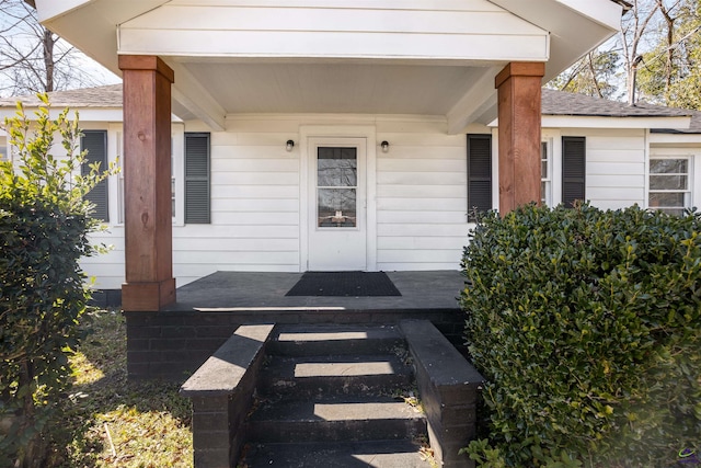 view of exterior entry featuring a porch and a shingled roof