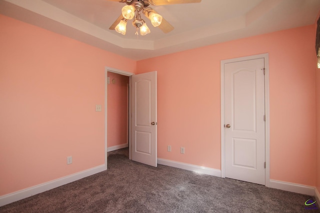 unfurnished bedroom featuring a tray ceiling, carpet flooring, ceiling fan, and baseboards