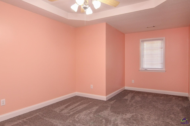 spare room featuring ceiling fan, dark carpet, a raised ceiling, and baseboards