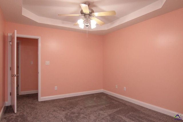 unfurnished room featuring ceiling fan, baseboards, dark carpet, and a raised ceiling