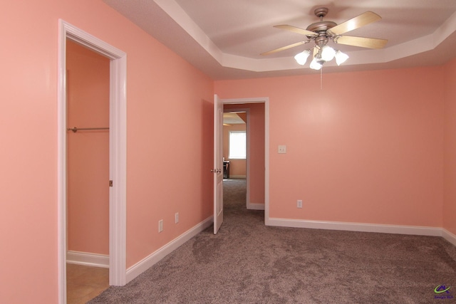 unfurnished bedroom featuring a tray ceiling, carpet flooring, ceiling fan, and baseboards
