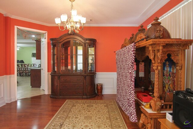 interior space featuring a wainscoted wall, crown molding, a notable chandelier, and wood finished floors