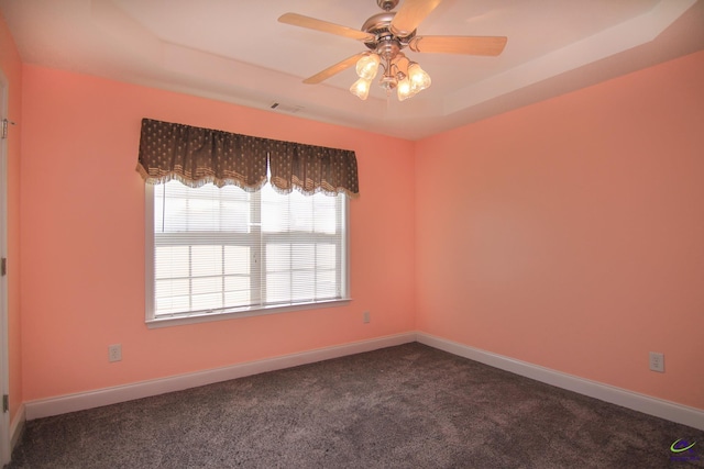 spare room with dark colored carpet, a tray ceiling, visible vents, and baseboards