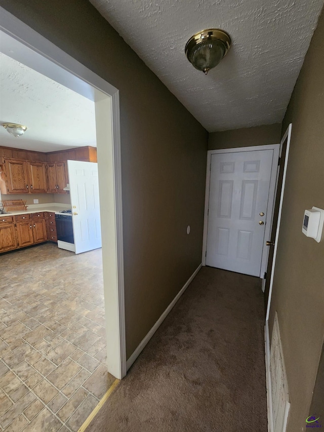 corridor with a textured ceiling, light colored carpet, visible vents, and baseboards