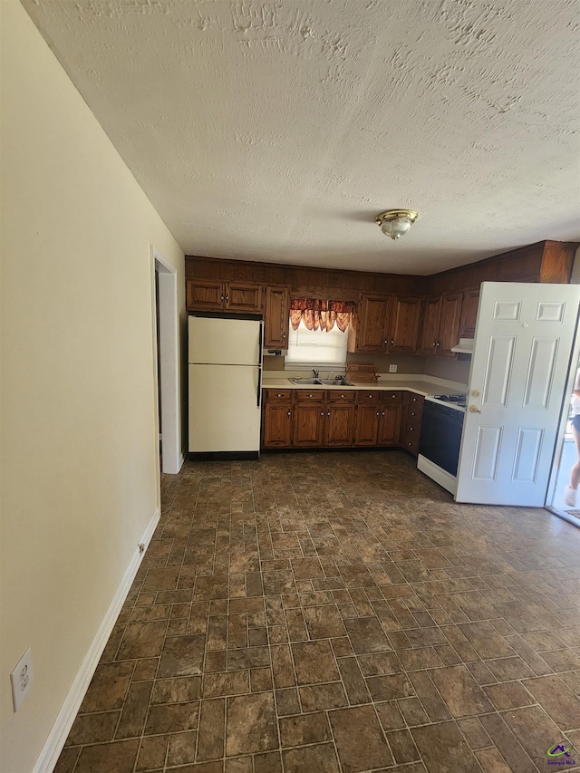 kitchen featuring a sink, baseboards, light countertops, freestanding refrigerator, and range with gas cooktop