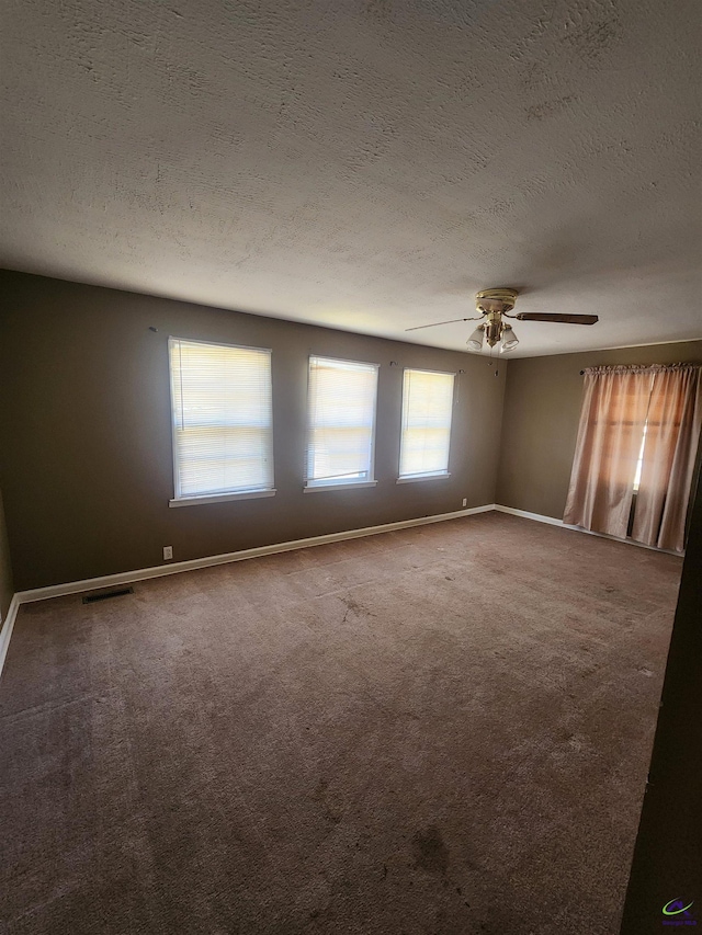 spare room featuring carpet floors, visible vents, a textured ceiling, and baseboards