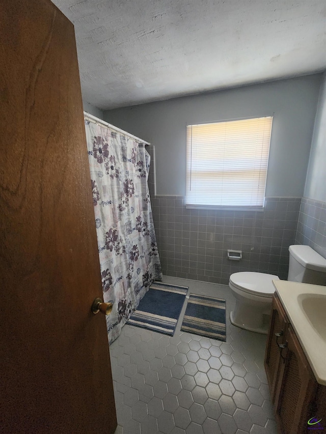 full bathroom featuring toilet, a wainscoted wall, tile patterned floors, tile walls, and a shower with curtain