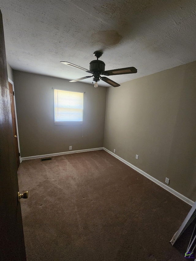 empty room with a textured ceiling, dark carpet, a ceiling fan, and baseboards