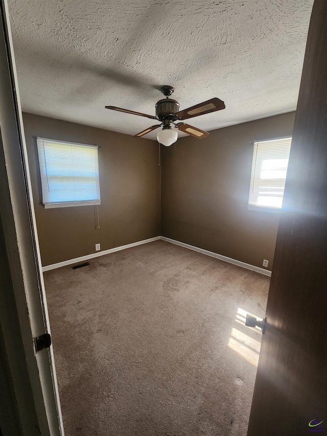 carpeted spare room with visible vents, baseboards, ceiling fan, and a textured ceiling