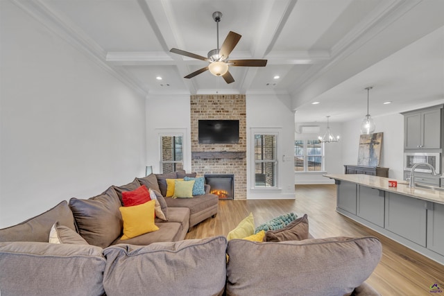 living area featuring light wood-style floors, a brick fireplace, beamed ceiling, and ceiling fan with notable chandelier