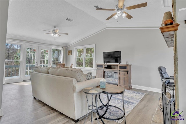 living area with a fireplace, visible vents, light wood-style flooring, ornamental molding, and vaulted ceiling