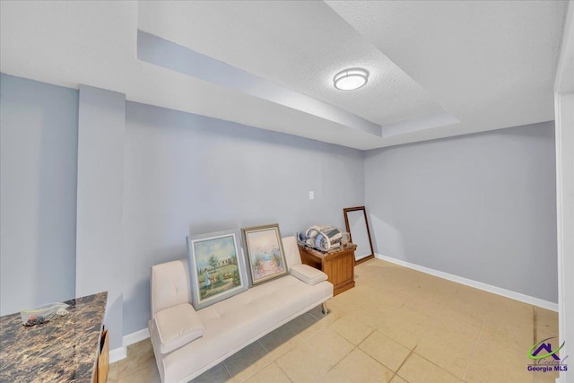 sitting room with a textured ceiling, a raised ceiling, and baseboards