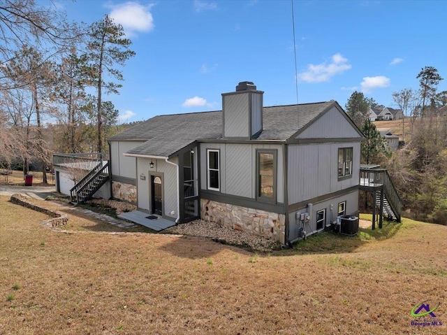 rear view of property featuring stone siding, central AC unit, stairway, and a lawn