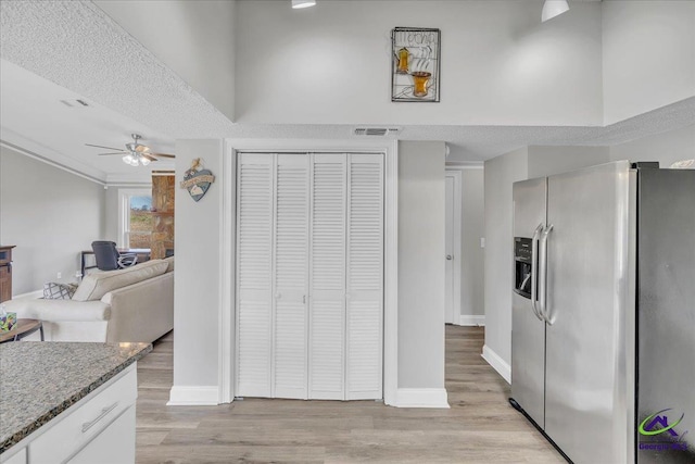 kitchen featuring light stone counters, light wood finished floors, visible vents, stainless steel fridge, and baseboards