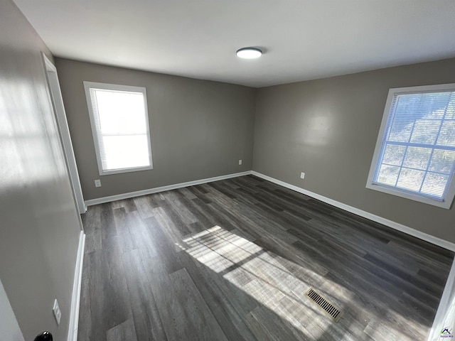 empty room with dark wood-type flooring, visible vents, and baseboards