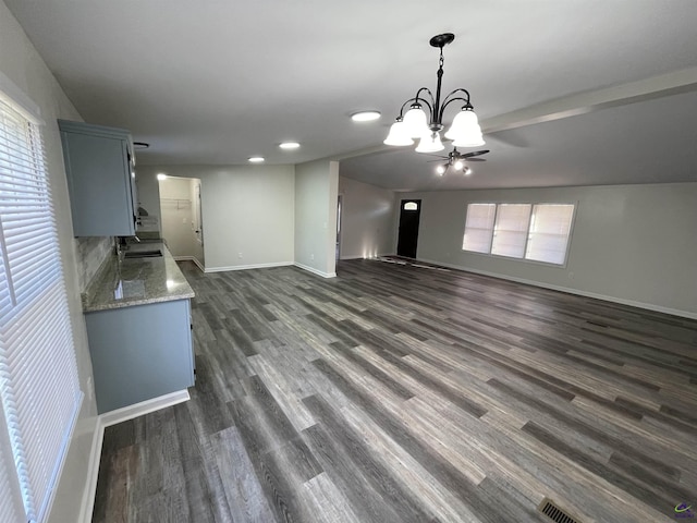 unfurnished living room with a notable chandelier, baseboards, and dark wood-style flooring