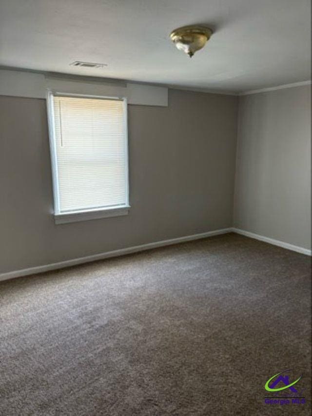 empty room with ornamental molding, carpet flooring, visible vents, and baseboards