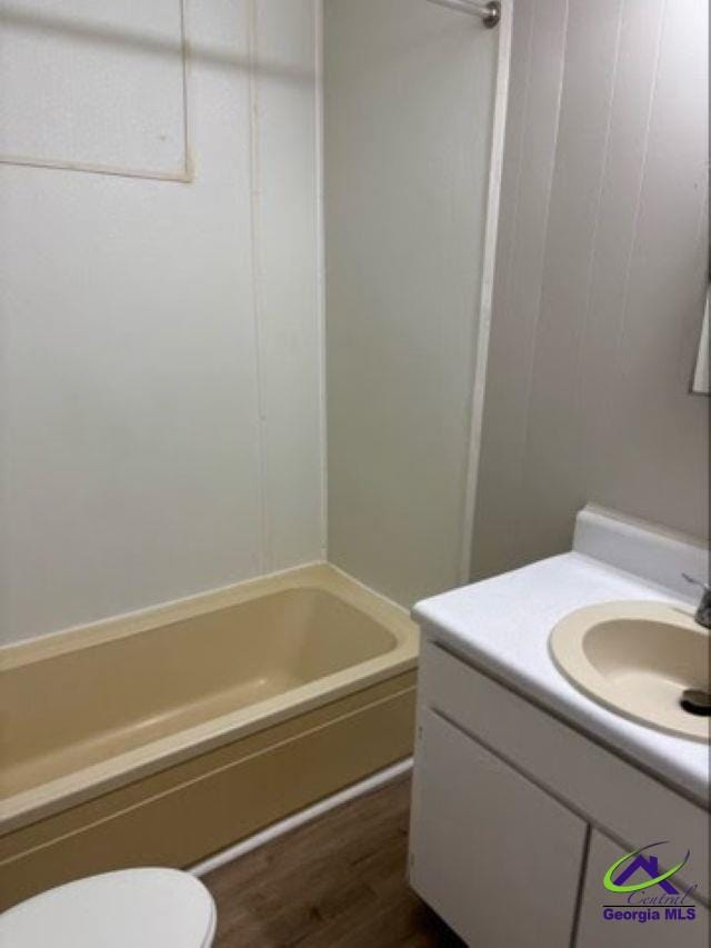 bathroom with toilet, shower / bathing tub combination, wood finished floors, and vanity