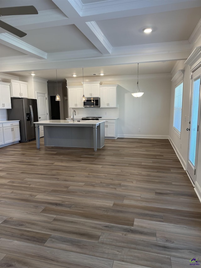 kitchen with a center island with sink, dark wood finished floors, appliances with stainless steel finishes, white cabinetry, and beam ceiling