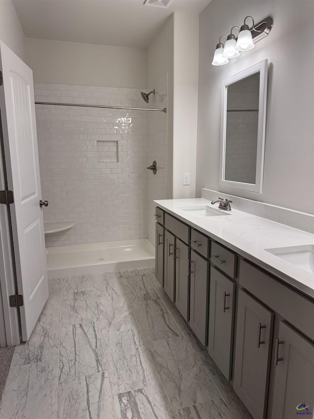 bathroom featuring marble finish floor, a sink, a tile shower, and double vanity