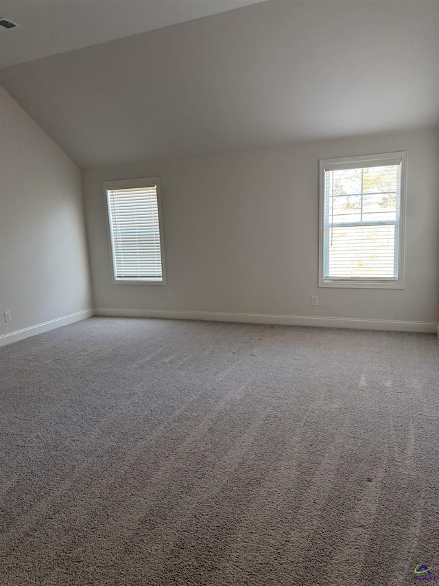 carpeted empty room with lofted ceiling, visible vents, and baseboards