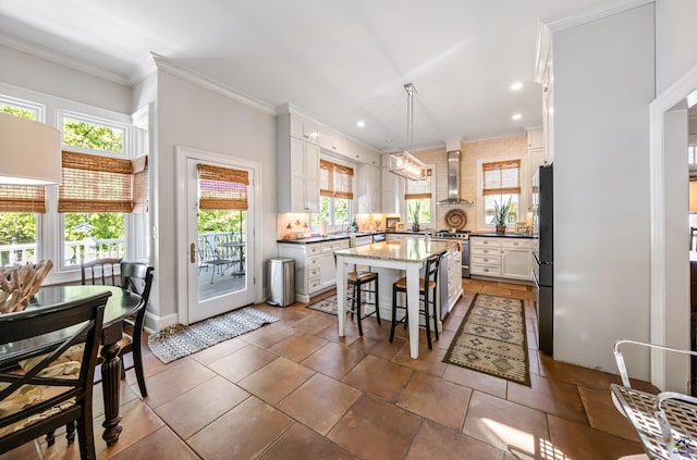 kitchen featuring a center island, crown molding, appliances with stainless steel finishes, white cabinets, and wall chimney range hood