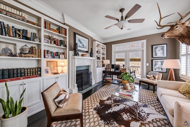 living room featuring ceiling fan, a fireplace with raised hearth, crown molding, and wood finished floors