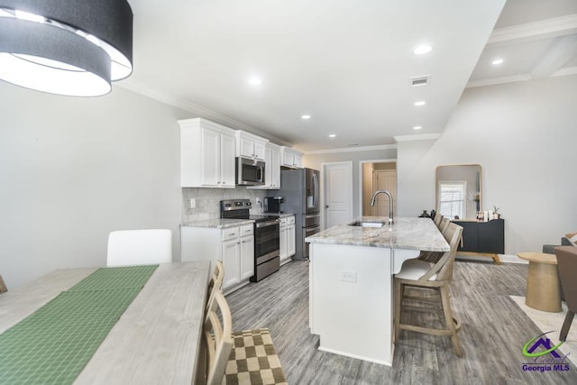 kitchen featuring stainless steel appliances, a sink, white cabinets, decorative backsplash, and a center island with sink