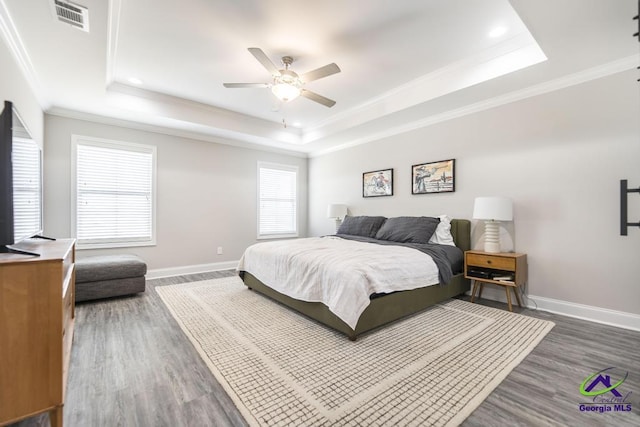 bedroom featuring baseboards, visible vents, a tray ceiling, and wood finished floors