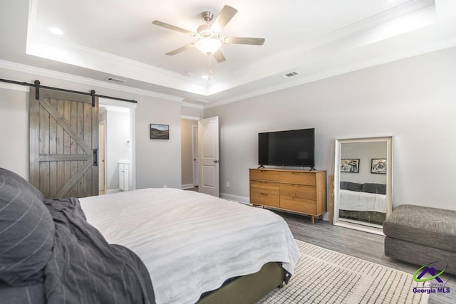 bedroom featuring a barn door, visible vents, ornamental molding, wood finished floors, and a tray ceiling