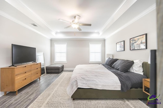 bedroom with wood finished floors, visible vents, a ceiling fan, a tray ceiling, and crown molding