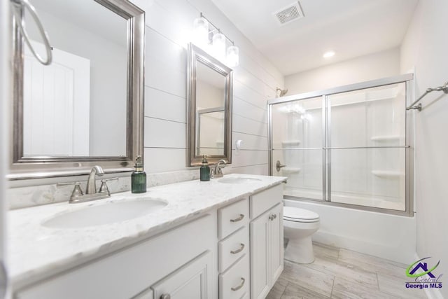 bathroom featuring double vanity, visible vents, toilet, combined bath / shower with glass door, and a sink