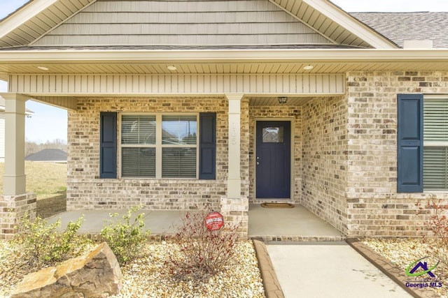 view of exterior entry with covered porch and brick siding