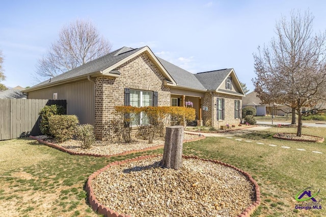 view of front of property featuring roof with shingles, fence, a front lawn, and brick siding