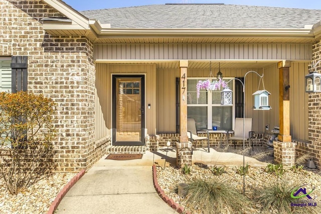 property entrance featuring covered porch, roof with shingles, and brick siding