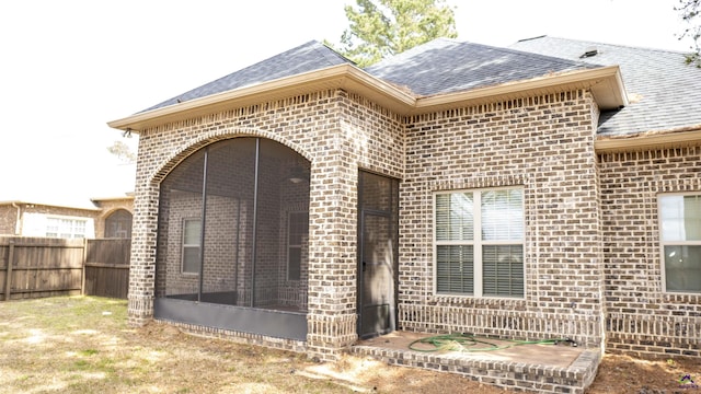 back of house with brick siding, roof with shingles, fence, and a sunroom