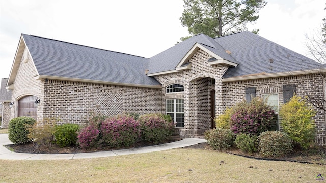 french provincial home featuring roof with shingles, a front yard, and brick siding