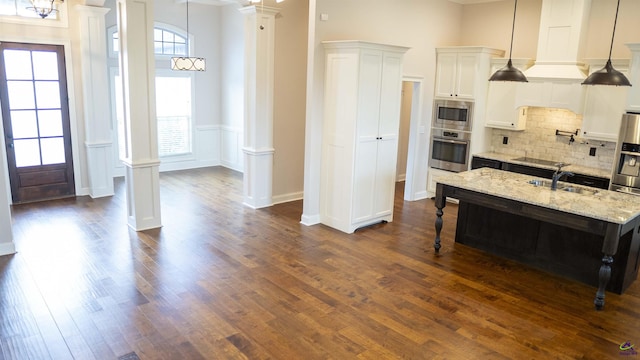 kitchen with ornate columns, a kitchen bar, stainless steel appliances, and dark wood finished floors