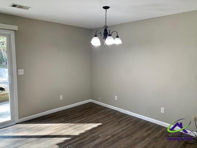 spare room featuring dark wood-style floors, a notable chandelier, visible vents, and baseboards