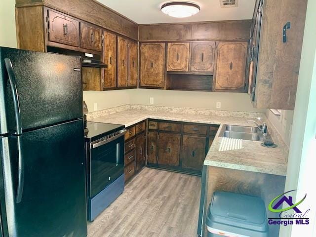 kitchen with stainless steel electric stove, light countertops, freestanding refrigerator, a sink, and light wood-type flooring