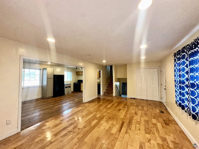 unfurnished living room featuring stairs, a textured ceiling, and light wood-style floors