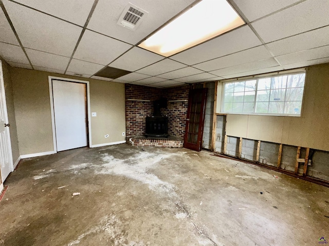 basement with a wood stove, a drop ceiling, visible vents, and baseboards