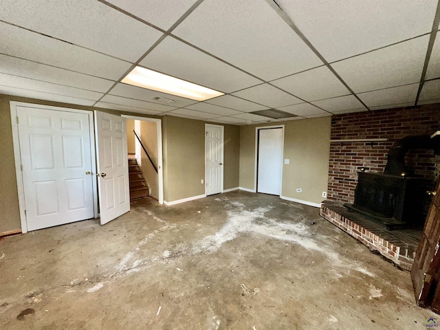 finished below grade area with a wood stove, a drop ceiling, baseboards, and stairs